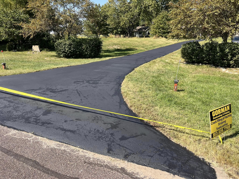 A long, newly sealcoated asphalt driveway by Gorman sealcoating & striping in Blue Springs, MO, with their service sign.