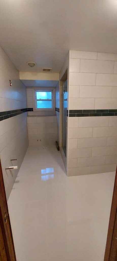 A long bathroom and shower area featuring new tile installation on walls and floor by True Alchemy - Tile & Grout Restoration in Denver, CO.