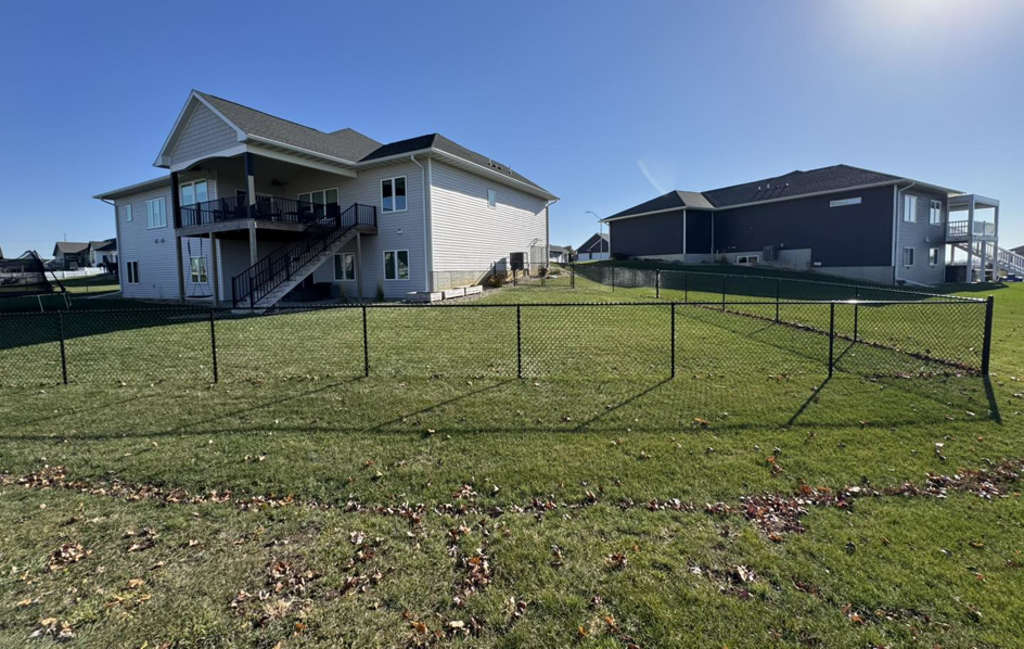 A long stretch of black chain-link fence defining a property line in a residential area, installed by Bergmann Fencing Co. in Cedar Falls, IA.
