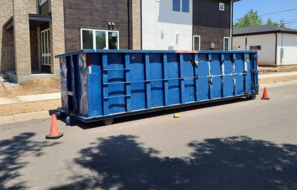 A long blue dumpster placed on a street with traffic cones, ready for debris at a construction site by Massie Dumpster Rental in Las Vegas, NV.