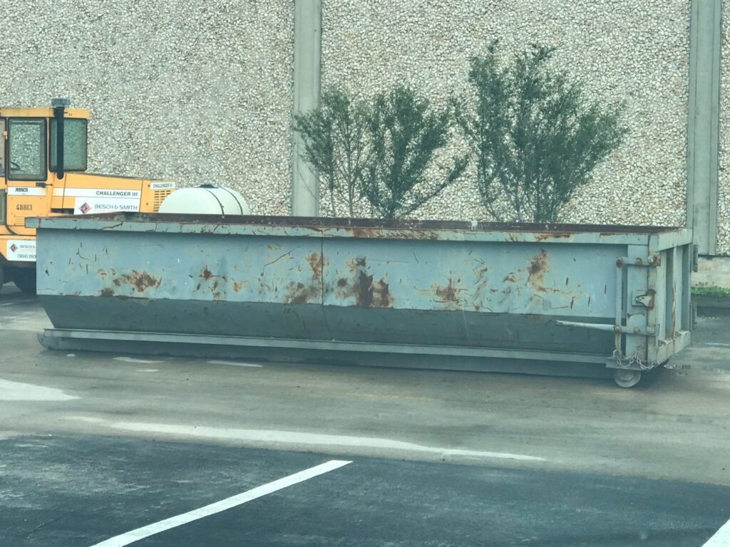 A long, empty gray roll-off dumpster, available for general junk removal projects from Waste Master Dumpster Rental Orlando, FL.