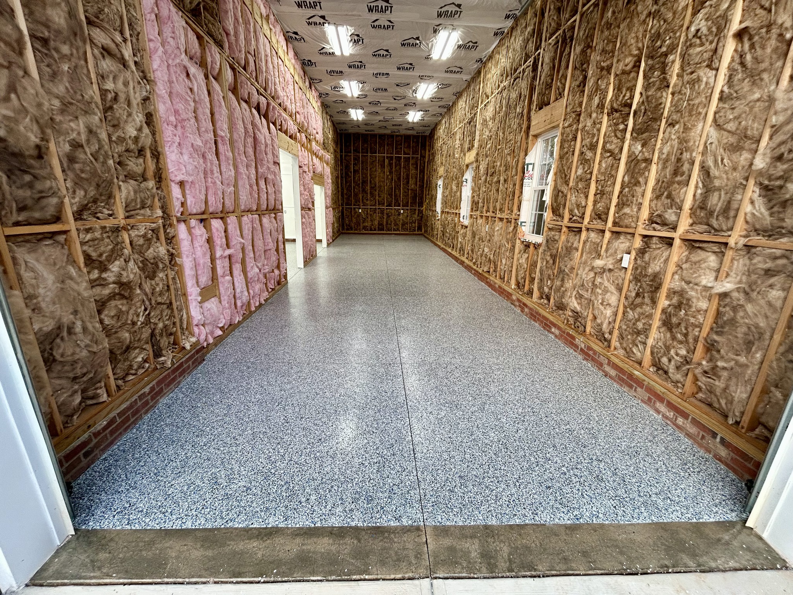 A long garage with a new speckled floor coating and unfinished walls by Garage Upgrade Pros in Fort Mill, SC.