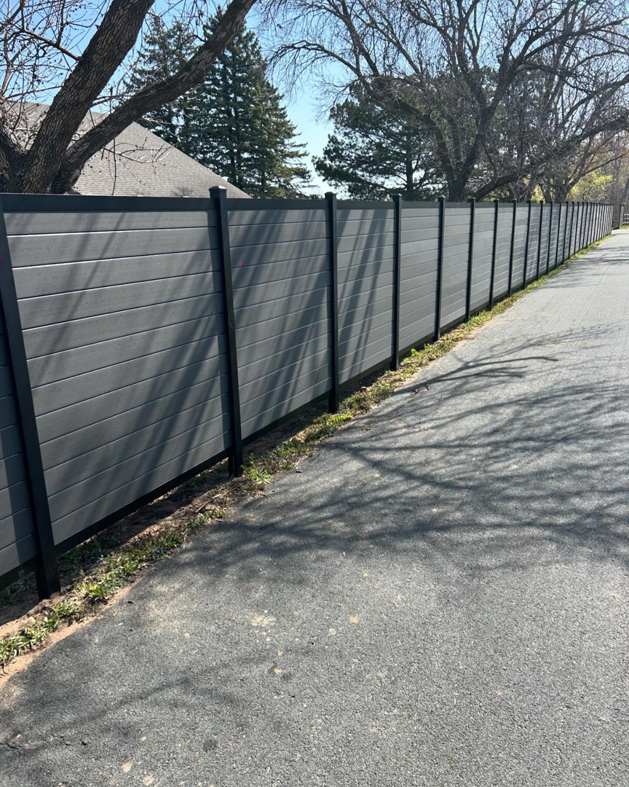 A long grey privacy fence installed alongside a paved path by Cyclone Fence in Somerset, WI.