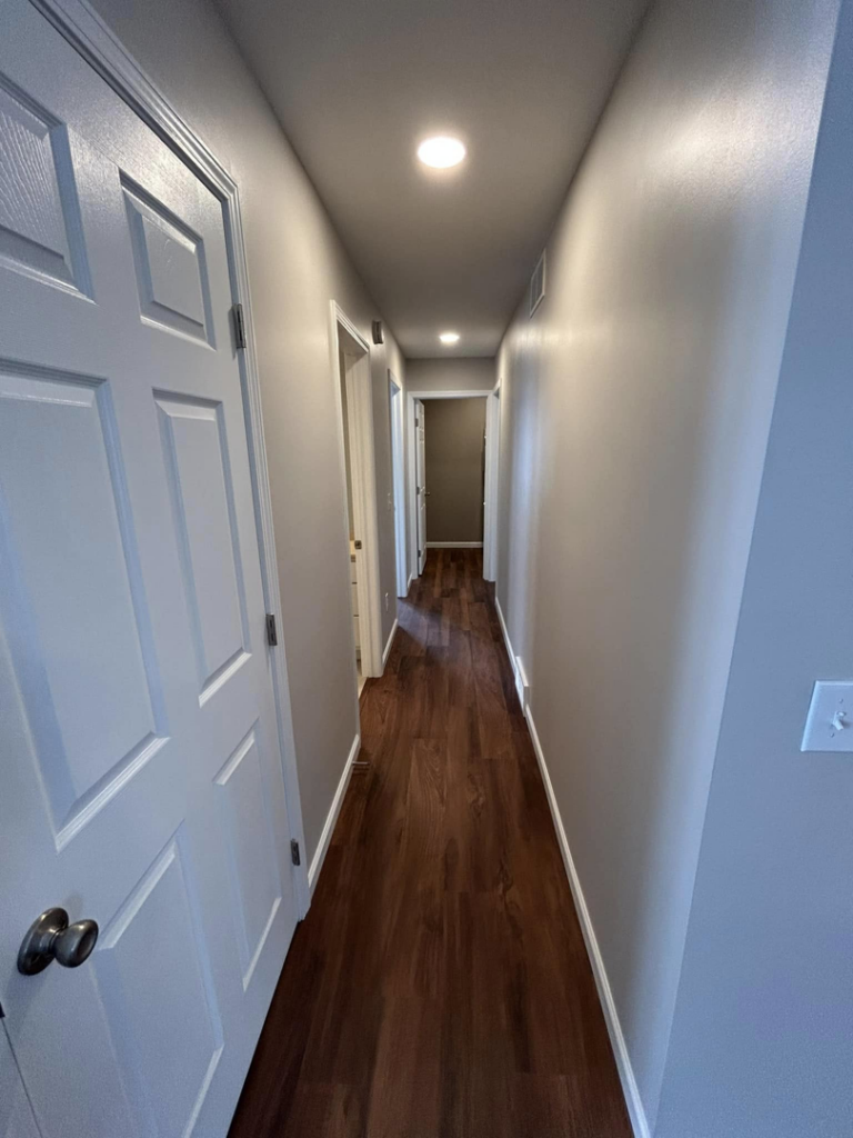 A long, bright hallway with new hardwood floors and recessed lighting, completed by Rock Solid Construction in Rochester, NY