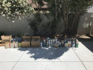A long line of paint cans and various hazardous waste items arranged for pickup by Hazawaytoday.com in El Segundo, CA
