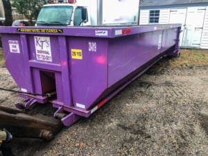 A long purple 20-yard dumpster from KT's Disposal on a gravel lot, indicating junk removal services in Hampton, VA.