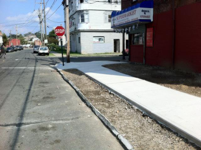 A long stretch of newly installed concrete sidewalk along a street, completed by Camelot Development in Bridgeport, CT.
