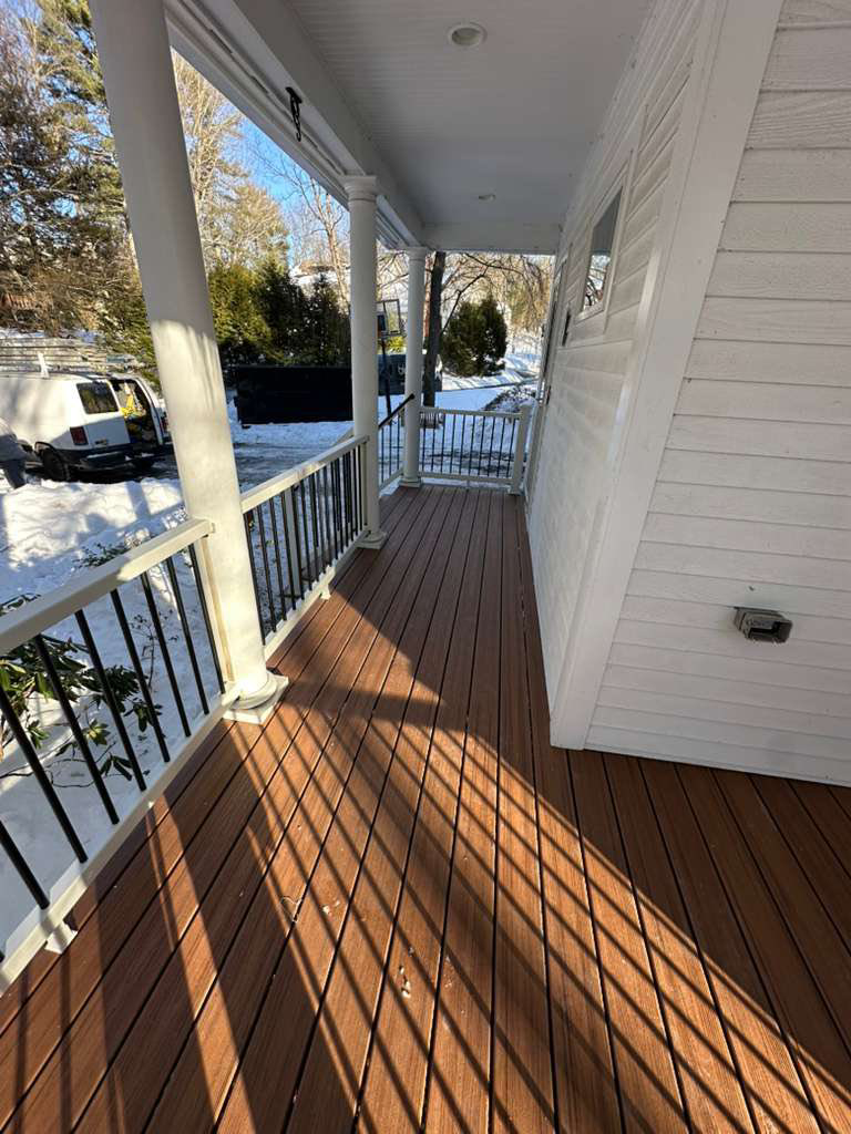 A long view of a newly constructed porch featuring composite decking, white columns, and railings, built by Remodel or Renew Home Improvement in Worcester, MA.
