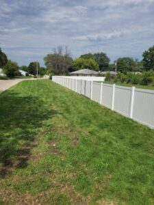 A long white vinyl fence installed along a grassy area next to a road by Badger Vinyl Products in Madison, WI.
