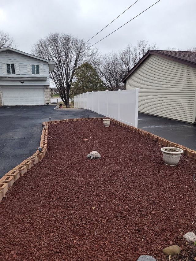 A long white vinyl privacy fence installed along a driveway and garden bed by Badger Vinyl Products in Madison, WI.
