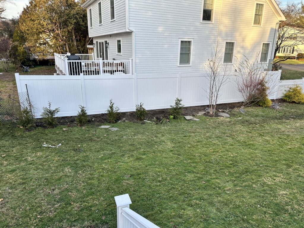A long white vinyl privacy fence installed along a residential property line by Fence Factory Inc in Stamford, CT