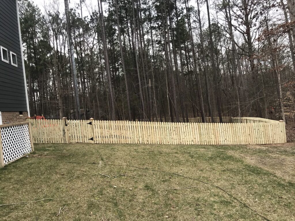 A long wooden picket fence with a gate installed in a backyard by Premier Fence Company in Glen Allen, VA.