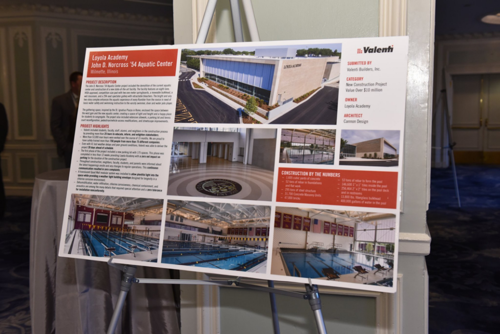 A display board showcasing the completed Loyola Academy Aquatic Center project by Valenti Builders, Inc. in Chicago, IL, featuring project details and photos.