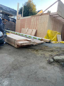 A stack of lumber delivered for a construction project with a worker on site by Mode Contracting in Seattle, WA.