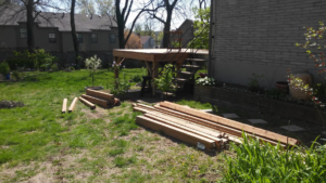 Lumber laid out on a lawn next to a partially constructed wooden deck, indicating a home improvement project by I'll Fix It in Shawnee, KS.
