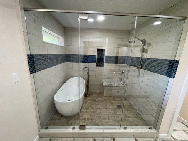 A luxurious bathroom remodel with a freestanding tub and a large glass shower by MC Master Construction in League City, TX