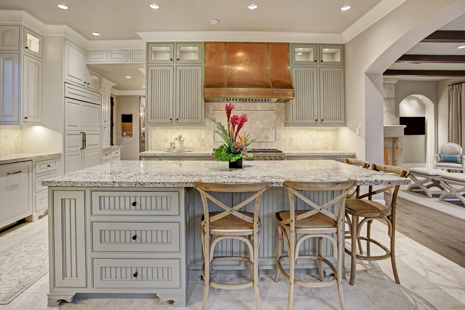 A luxurious kitchen interior with a large island, custom cabinetry, and a distinctive copper range hood by Allan Edwards Builder Inc in Houston, TX.