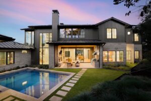 A luxurious modern home exterior at dusk, showcasing a swimming pool and an illuminated patio by Stone Acorn Builders in Bellaire, TX.