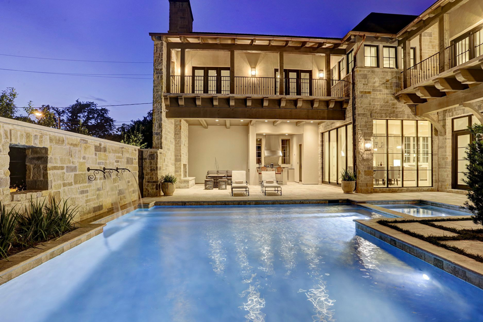 A luxurious stone house exterior with a large swimming pool and outdoor living area at dusk, built by Allan Edwards Builder Inc in Houston, TX.