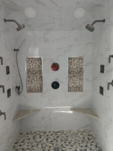 A luxurious walk-in shower with multiple shower heads, tiled walls, and a pebble floor by Santoro Home Improvements in Wallingford, CT.