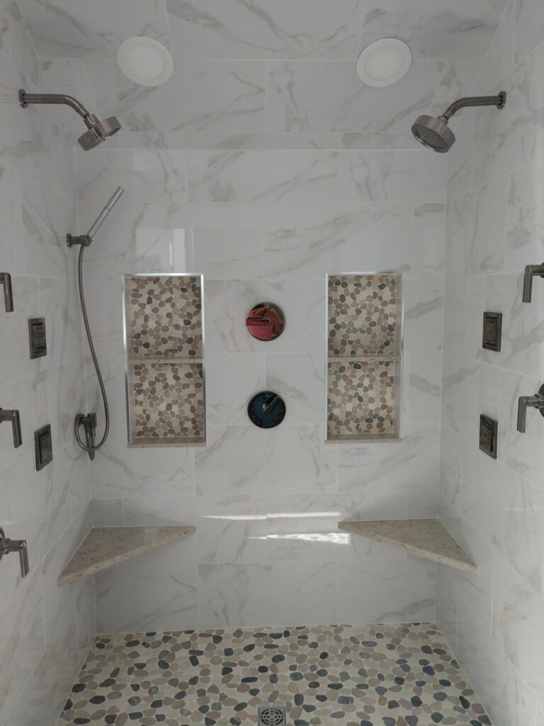 A luxurious walk-in shower with multiple shower heads, tiled walls, and a pebble floor by Santoro Home Improvements in Wallingford, CT.