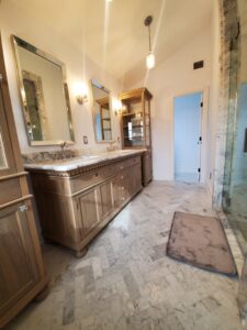 Luxury bathroom with marble herringbone floor and custom wood vanities by APJ Construction Inc. in El Paso, TX.