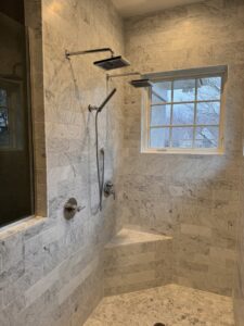 A luxurious walk-in shower with marble-look tiles, multiple shower heads, and a built-in bench by Inova Builds in Bloomington, MN.