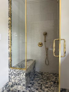 A luxurious bathroom shower with marble accents and gold-framed glass doors installed by Kyle Build in Chattanooga, TN.