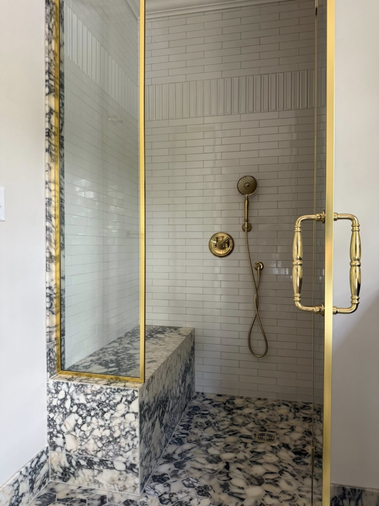 A luxurious bathroom shower with marble accents and gold-framed glass doors installed by Kyle Build in Chattanooga, TN.