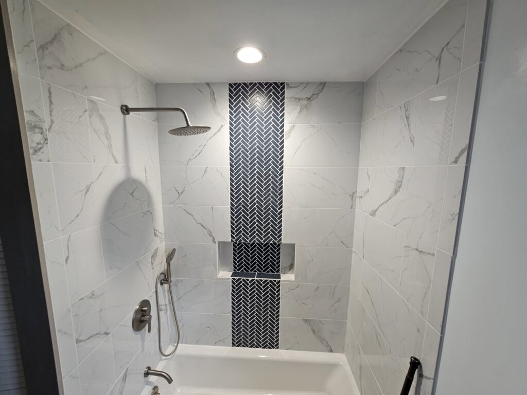 A luxurious completed bathroom shower remodel with marble-look tiles and a herringbone accent by Ben Nye The Fix-It Guy in Erie, PA.