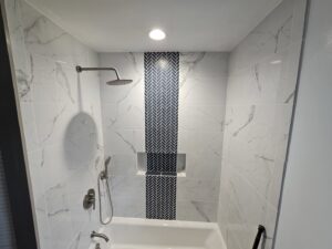 A luxurious completed bathroom shower remodel with marble-look tiles and a herringbone accent by Ben Nye The Fix-It Guy in Erie, PA.