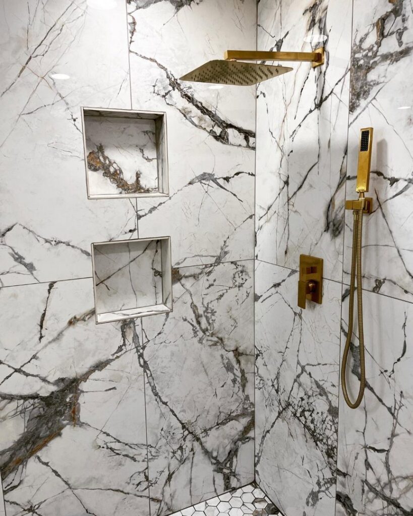 A luxurious shower renovation featuring gold fixtures, large format marble-look tiles, and dual niches by J.C.Improvement in Katy, TX.