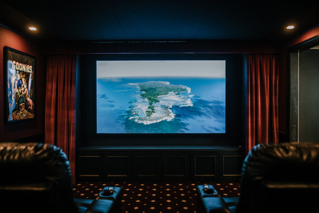 A luxurious home theater room with a large screen, red curtains, and comfortable recliners designed by Knaub Home Solutions in Rochester, NY.