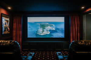 A luxurious home theater room with a large screen, red curtains, and comfortable recliners designed by Knaub Home Solutions in Rochester, NY.