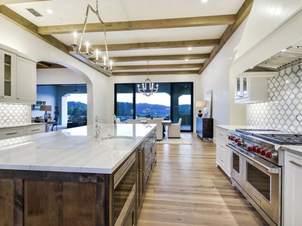 A luxury kitchen design with exposed wooden beams and a large marble island by Stone Age Granite of Austin, TX.