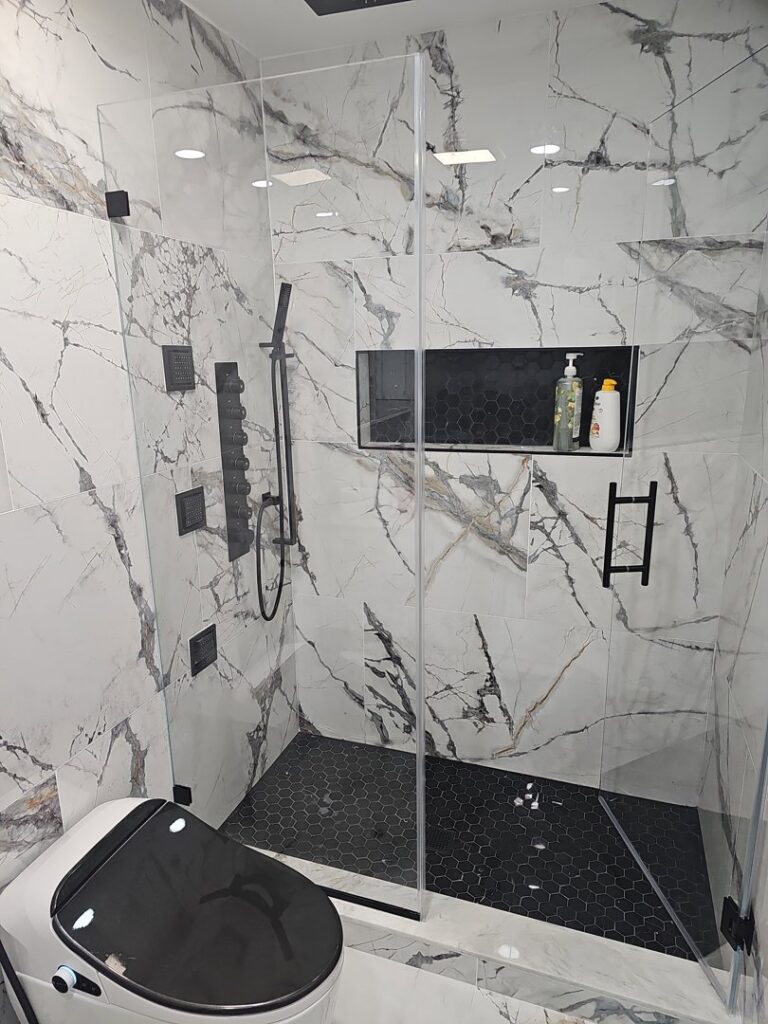 A luxury bathroom shower remodel featuring marble-look tiles and a modern black shower system by Luis handyman service in Albuquerque, NM