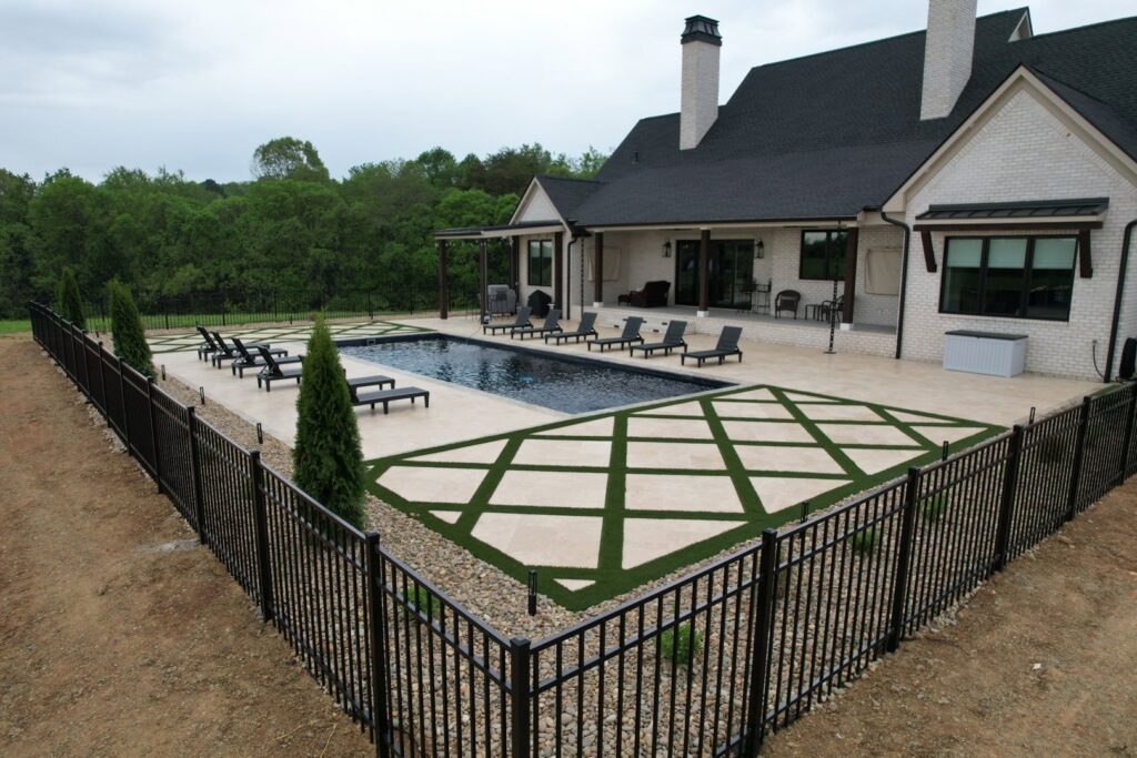 A luxurious backyard pool area with a large stone patio and decorative artificial turf installed by Southern Pool Solutions in Knoxville, TN.