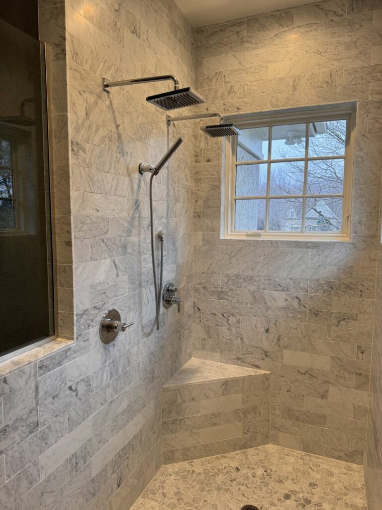 A luxurious walk-in shower with multiple showerheads, marble-look tiles, and a built-in bench, installed by Inova Builds in Bloomington, MN.