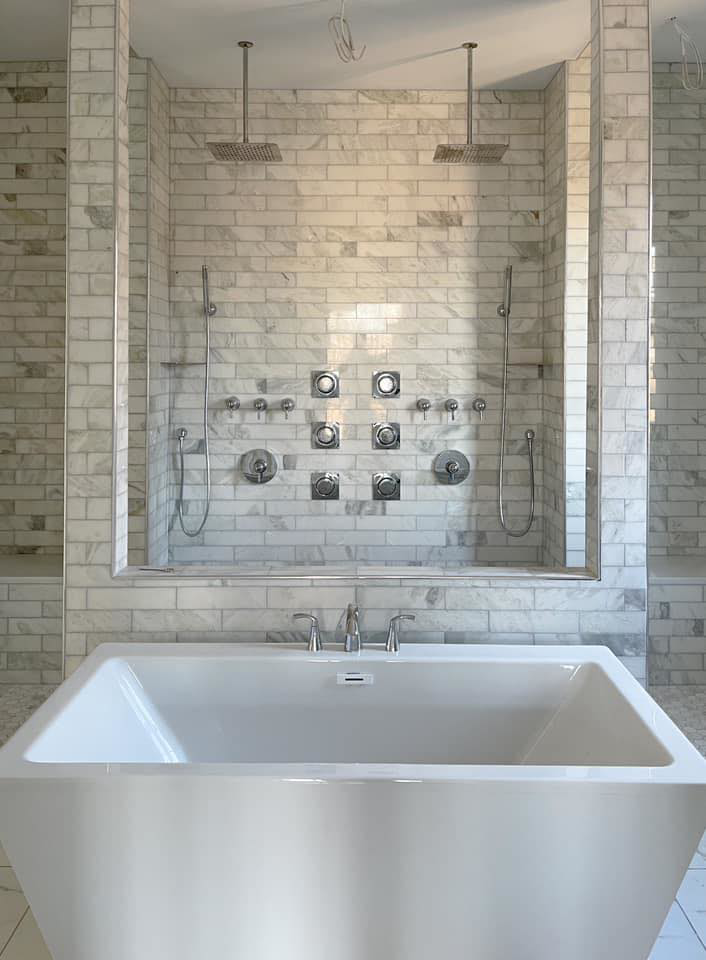 A luxurious tiled bathroom featuring a freestanding tub and a large shower with multiple heads by Clean Cut Tile LLC in St. Louis, MO.