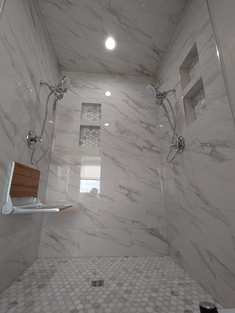 A luxurious tiled shower with dual shower heads, a built-in bench, and hexagonal floor tiles, completed by Devco Construction LLC in West Valley City, UT