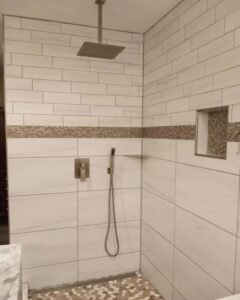 A luxurious walk-in shower with a rain shower head, decorative accent tile, and a pebble floor, installed by Ace Tile & Finishing LLC in Philadelphia, PA.