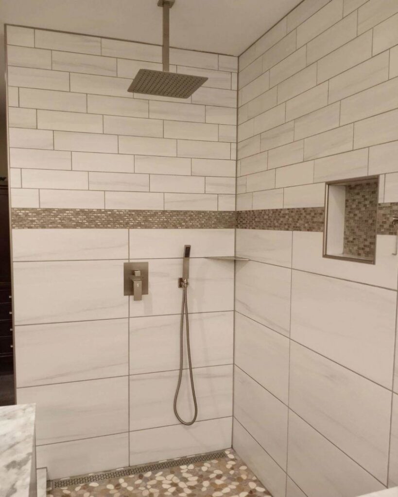 A luxurious walk-in shower with a rain shower head, decorative accent tile, and a pebble floor, installed by Ace Tile & Finishing LLC in Philadelphia, PA.