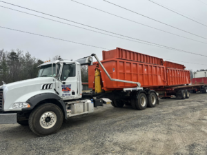 A Mack Daddy Dumpsters truck hauling multiple orange dumpsters on a trailer, providing junk removal services in Winston-Salem, NC.