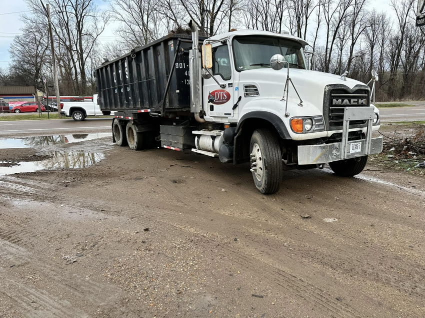 A Dts dumpster rentals Mack truck with an empty dumpster parked on muddy ground in Memphis, TN.