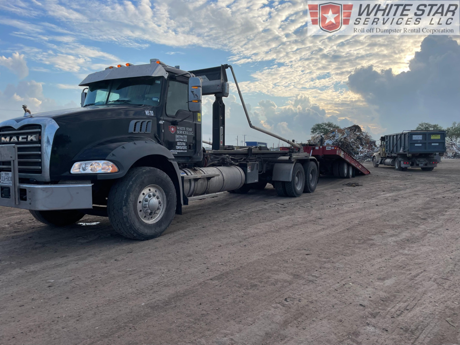 A Mack truck from White Star Services LLC hauling scrap metal on a trailer in Corpus Christi, TX, with another dumpster truck in the background.