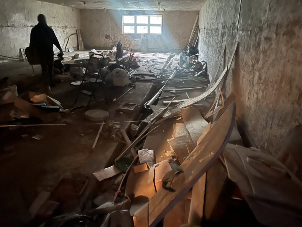 A makeshift shed with surrounding debris in a wooded area, representing a cleanout job for Tiny's Trash & Hauling Service L.L.C in Williamstown, VT