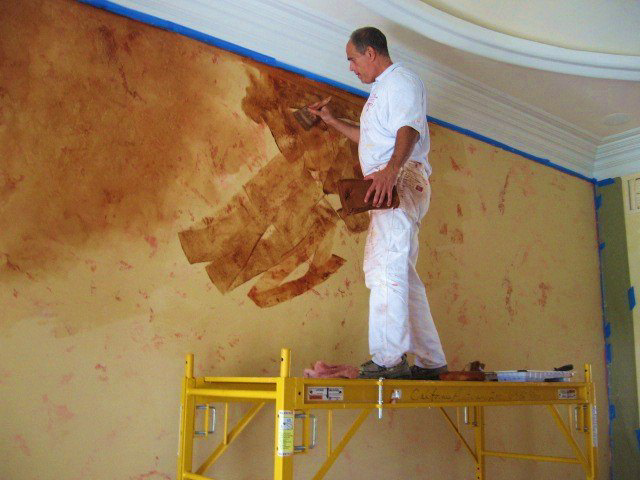 A man on scaffolding applying textured paint to a wall, a service by Sherrod Painting in Mobile, AL.
