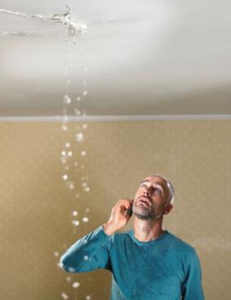 A man on the phone looking up at a leaking ceiling, indicating water damage needing repair from KC Water Damage in Kansas City, MO.