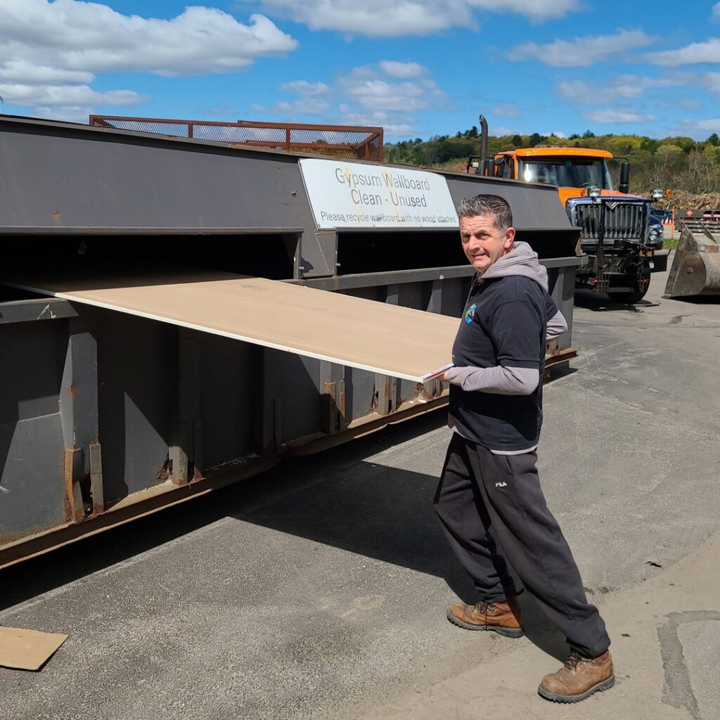 A Green Clover team member carrying a sheet of drywall to a dumpster for disposal in Quincy, MA.