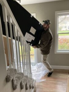 A man carrying a large panel down a staircase inside a home, a service provided by Hometown Hauling 802 in Milton, VT.